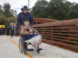 woman in a wheelchair crosses bridge with help from a man