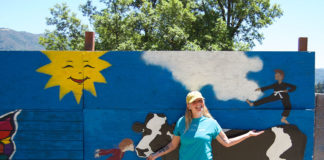 Woman standing outside in front of a large, free-standing mural that depicts a cow, a horse and a child