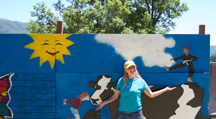 Woman standing outside in front of a large, free-standing mural that depicts a cow, a horse and a child