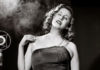 Black-and-white photo of woman in an evening gown by an old-fashioned microphone
