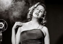 Black-and-white photo of woman in an evening gown by an old-fashioned microphone