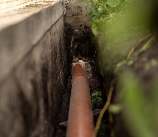 ORANGE PLASTIC This sewage pipe was laid inside a deep narrow trench along a concrete foundation wall. (Shutterstock)