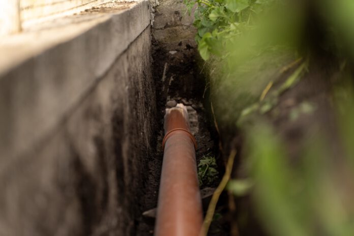 ORANGE PLASTIC This sewage pipe was laid inside a deep narrow trench along a concrete foundation wall. (Shutterstock)